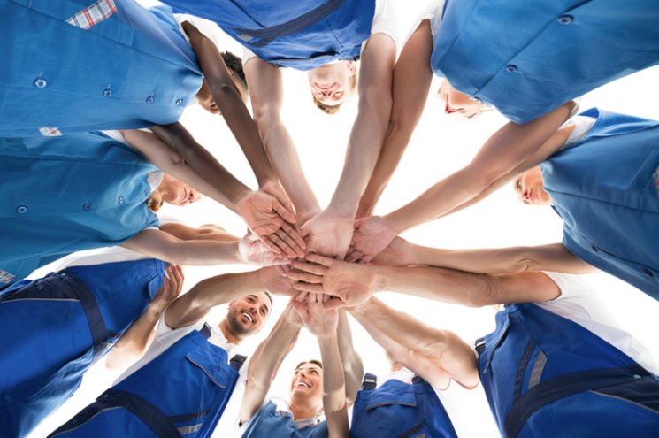 A team with hands stacked together in a huddle, ready to serve
